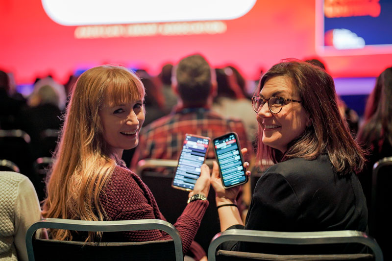 Two smiling women showing the LibLearnX Mobile App on their mobile phones.