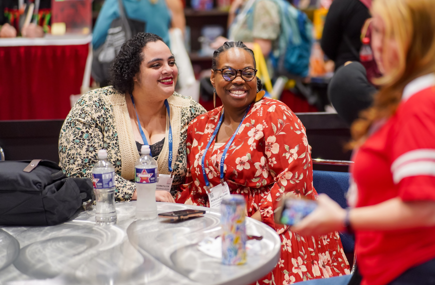 Two people posing for a photo at a table while others look on in the background.
